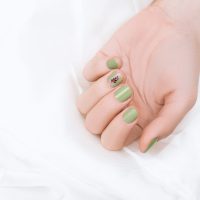 Green nail design with black tree art on middle finger. Manicured female hand.