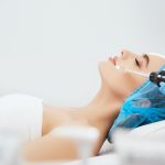 profile-smiling-woman-blue-cap-lying-couch-cosmetological-clinic-with-closed-eyes-doctor-s-hands-blue-gloves-doing-darsonvalization-procedure_355000-906